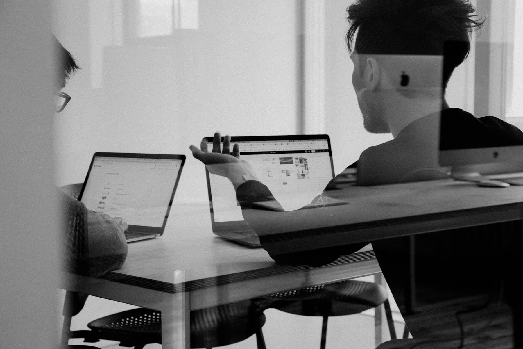Black-and-white photograph of two people working side by side at laptops