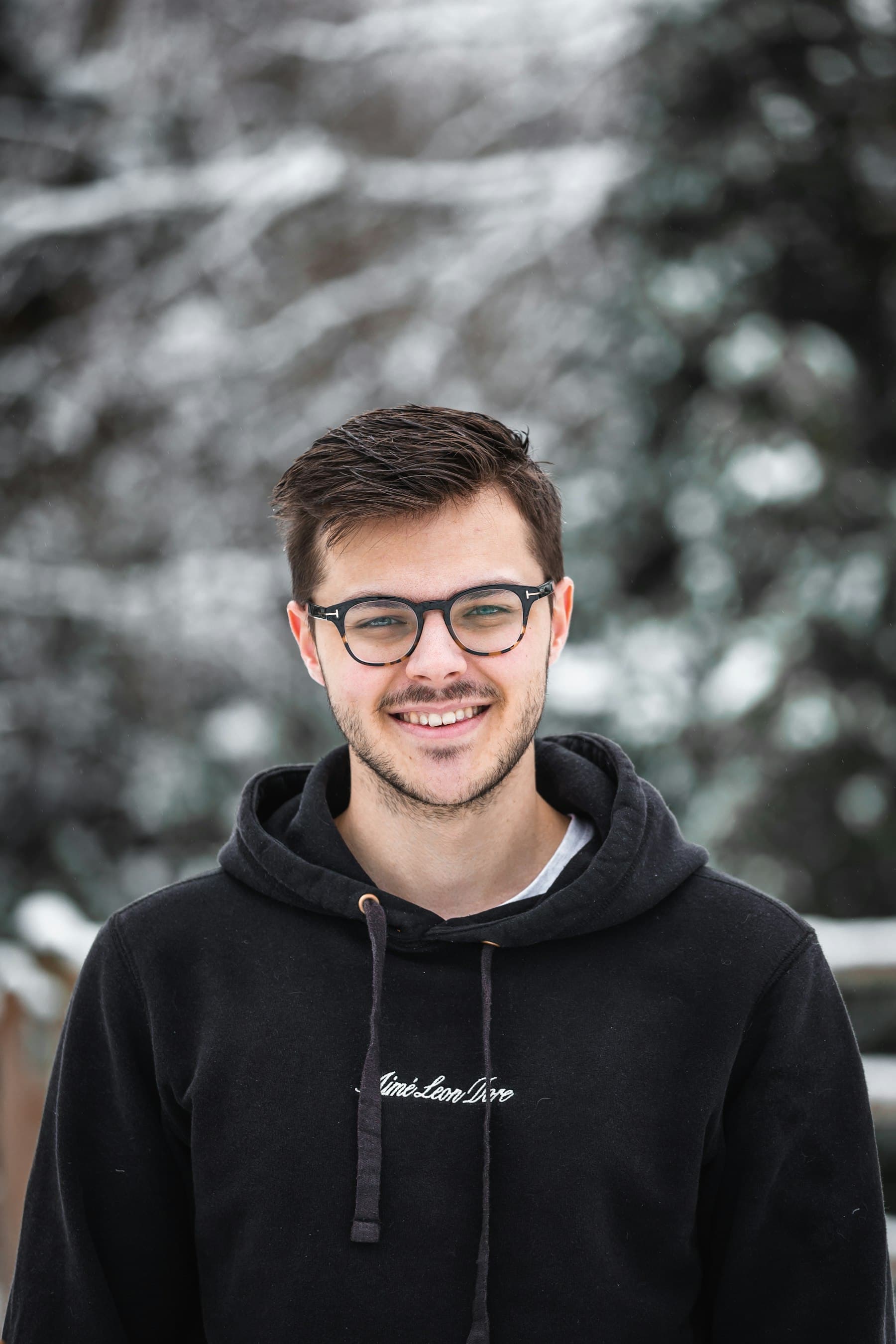 Smiling man in glasses and a dark hoodie outdoors