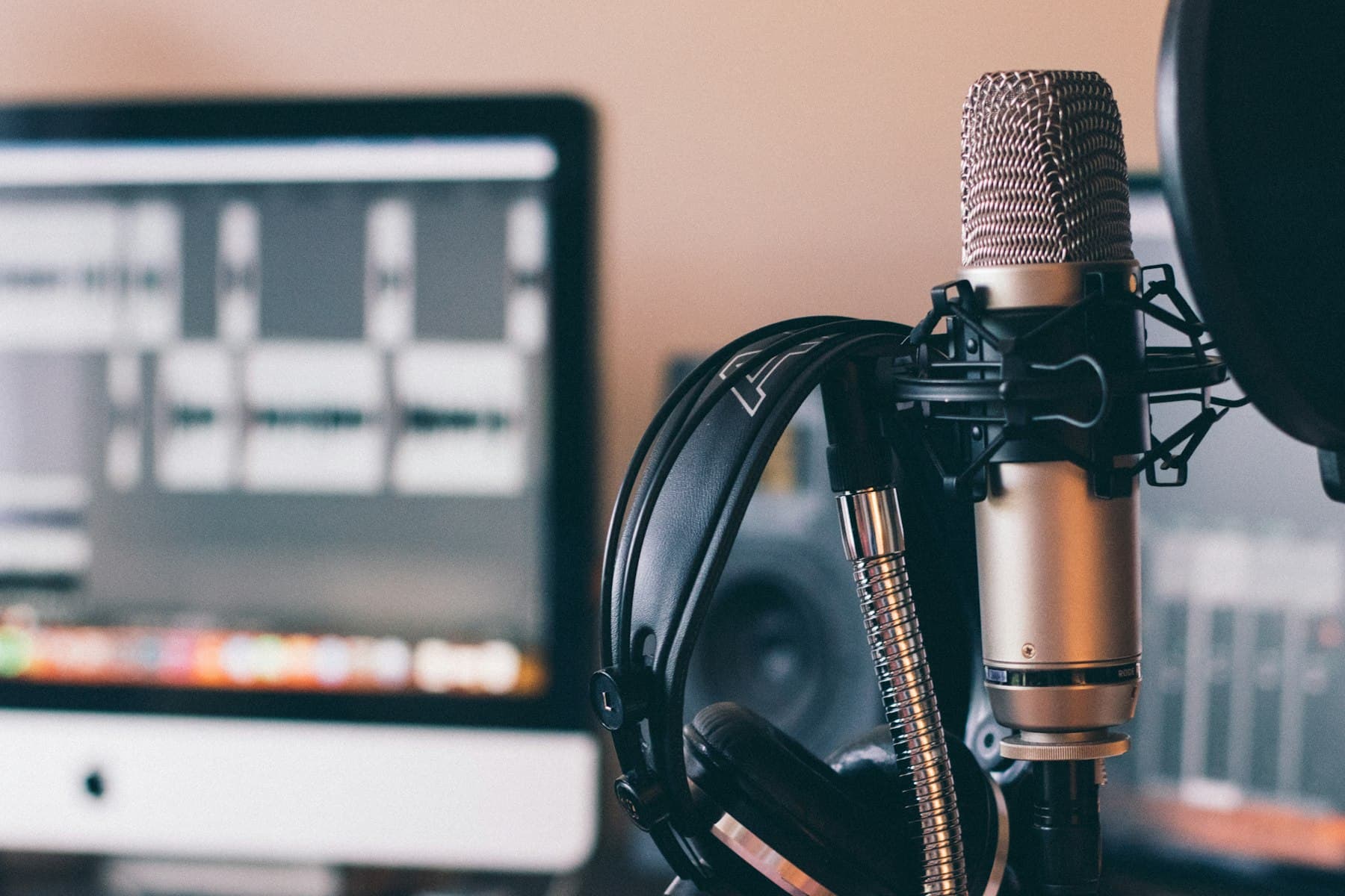 A microphone and headphones on a desk beside an editing screen